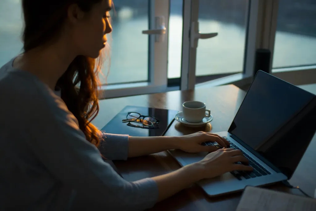 Frau tippt auf Laptop. Kaffe steht daneben